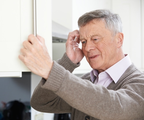 man looking confused as he looks into kitchen cabinet