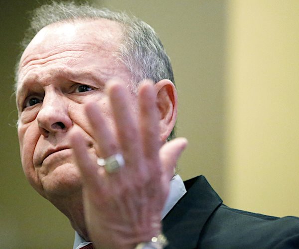 a dejected roy moore throws his left hand up helplessly, partially blocking his face