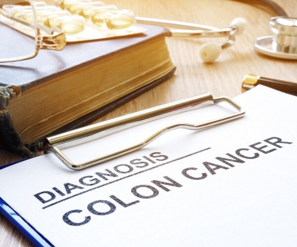 clipboard with colon cancer diagnosis next to a book, stethoscope, and pills