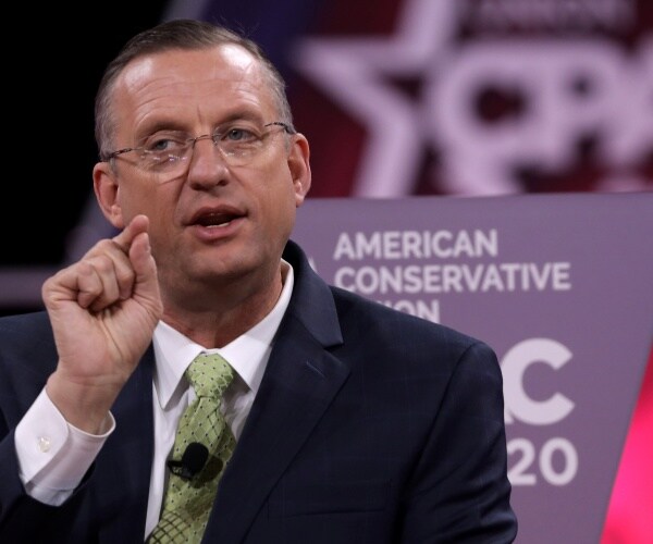 doug collins in a green tie and black suit speaking at cpac