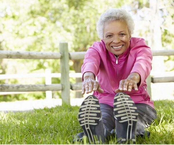 older woman outside sitting in grass stretching