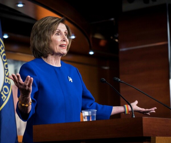 pelosi in a blue suit standing at a podium and speaking