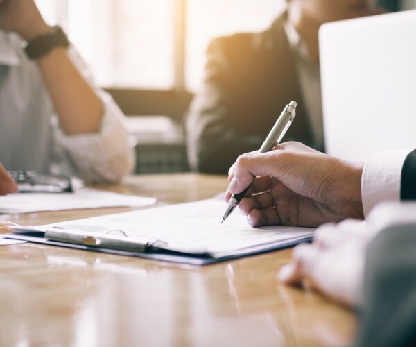 man writing on paper on clipboard in meeting