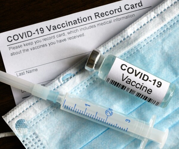 vial of COVID vaccine, syringe, mask, vaccine record card