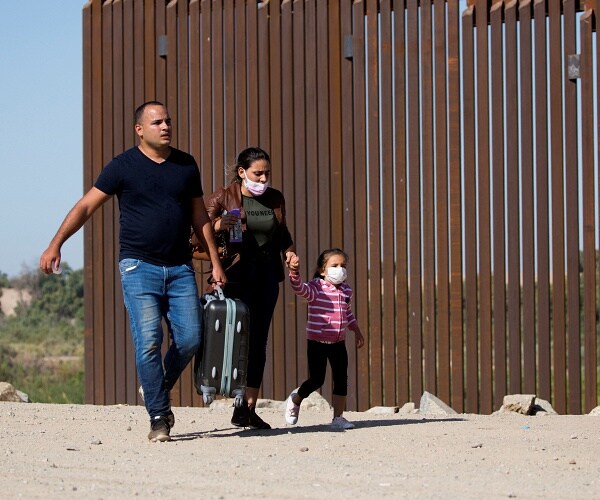 migrants walk past border wall