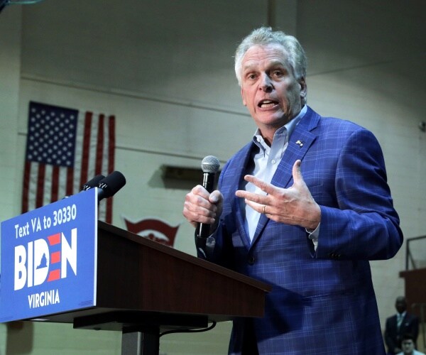 terry mcauliffe speaks at a podium with a biden sign