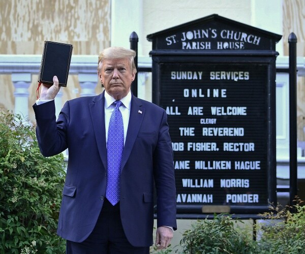 trump in a navy blue suit and blue tie holds a bible in his right hand in front of st john's church