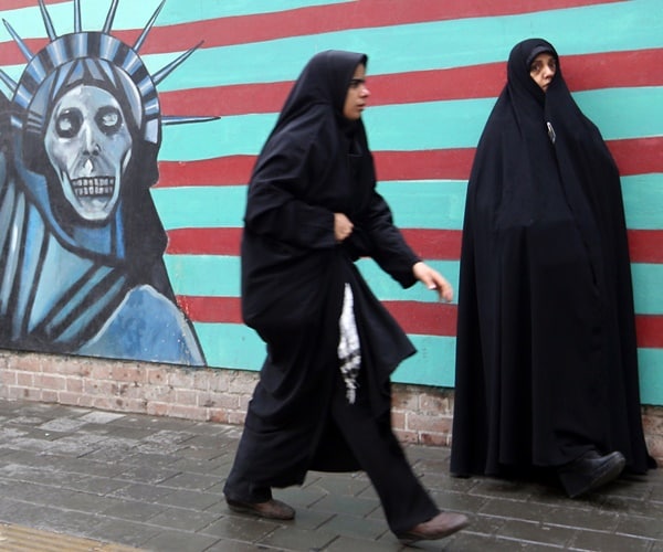 women in burkas walk past a ghoulish statue of liberty mural.