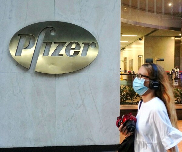 woman walks by pfizer wearing mask