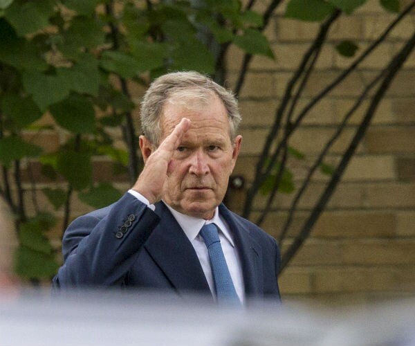 former president george w. bush is shown in suite and tie, giving a salute