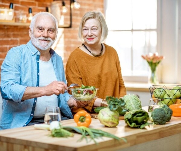 Man and woman in kitchen preparing a meal with vegetables and fruit