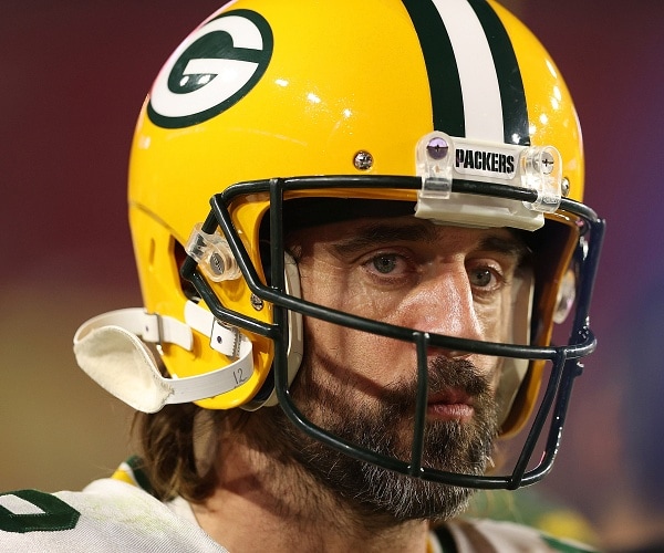 aaron rodgers stands on field wearing helmet