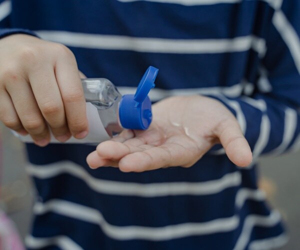 person wearing a white and blue striped shirt squirting hand sanitizer into their palm