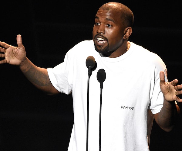 kanye west wears a white house and speaks into a mic during a stand-up routine