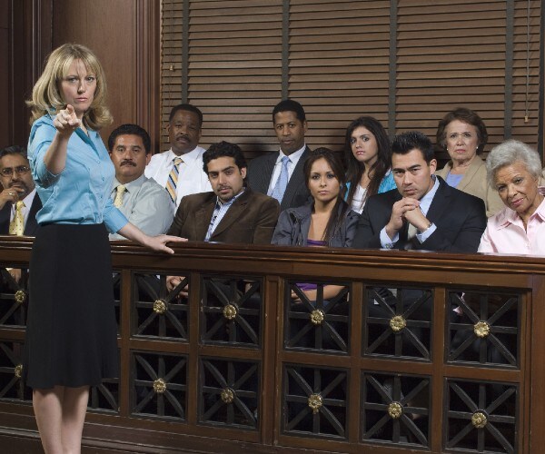 a prosecutor stands in front of a jury and points toward the camera