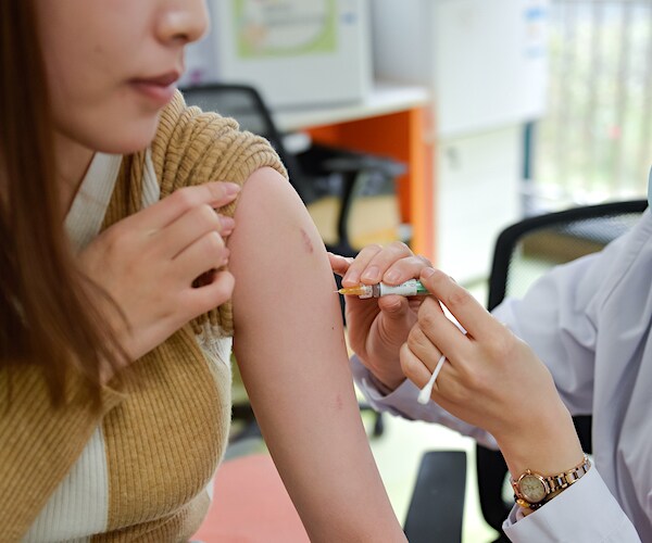 a woman holds up her left sleeve as she takes a shot of a vaccination