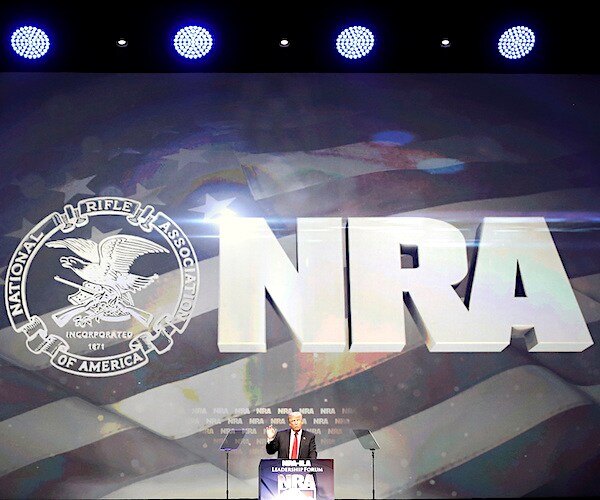 the logo for the national rifle association is spread across the top of the stage as the president delivers a speech