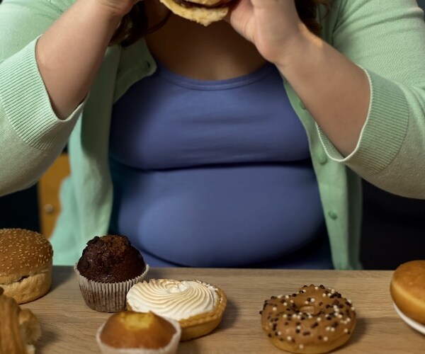 overweight woman stress eating with lots of sugary, unhealthy foods in front of her