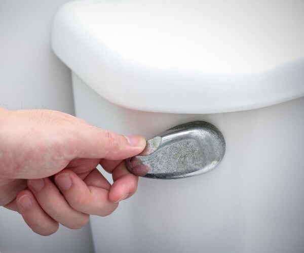 close up of person's hand on toilet flusher 