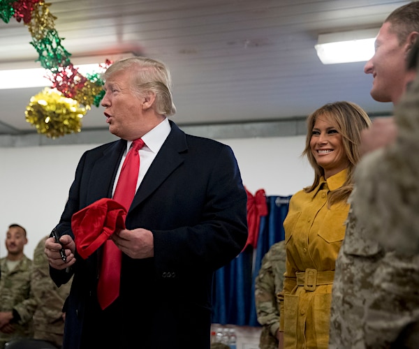 president donald trump holds a black marker and a red maga hat while smiling during a christmastime visit with troops