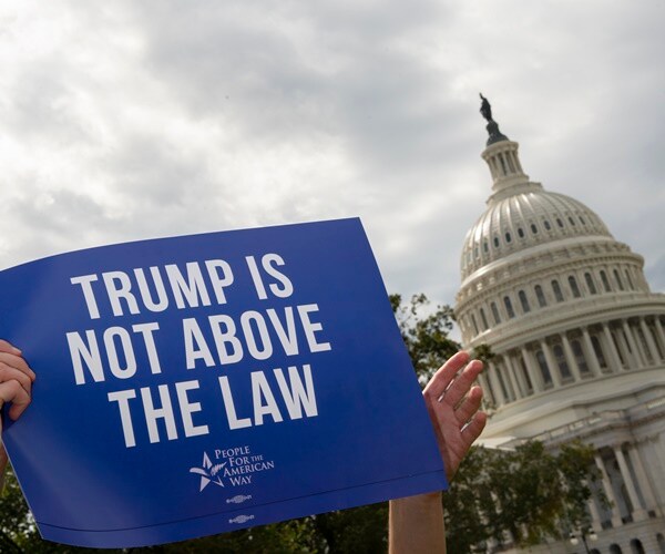 a sign to impeach is held up with the capitol dome in the background