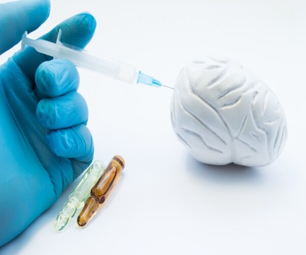 model of a brain, with a syringe with medication injecting into it