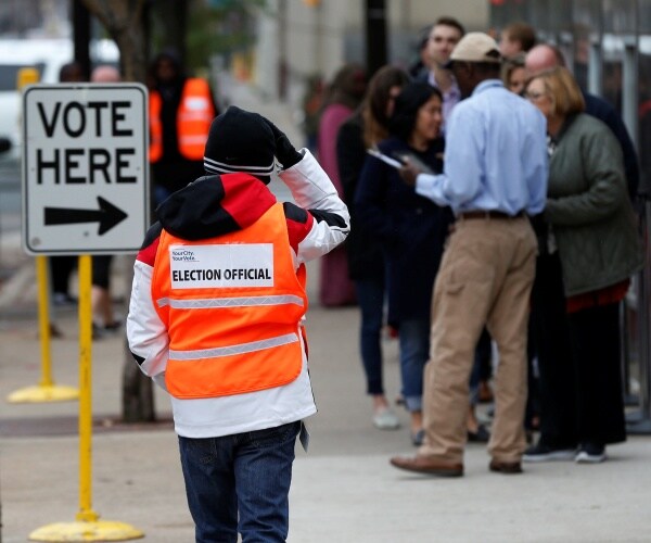 An election official maintains the crowd line and parking spaces as people line up to vote