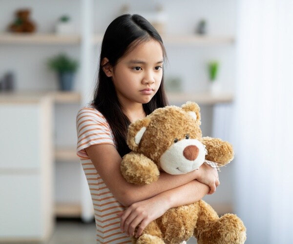 young girl looks sad while holding a teddy bear