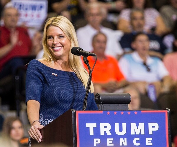 pam bondi smiles at a podium at a jacksonville rally.