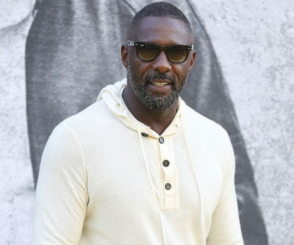 idris elba is shown wearing a cream shirt and black trousers and sunglasses