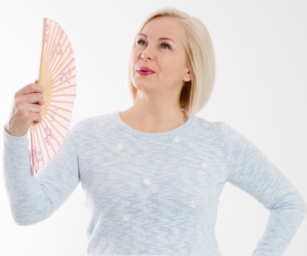 middle aged woman having a hot flash, using fan to cool herself