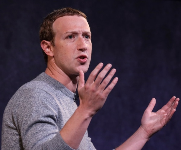 zuckerberg in a gray long sleeve t shirt speaking with his arms held up