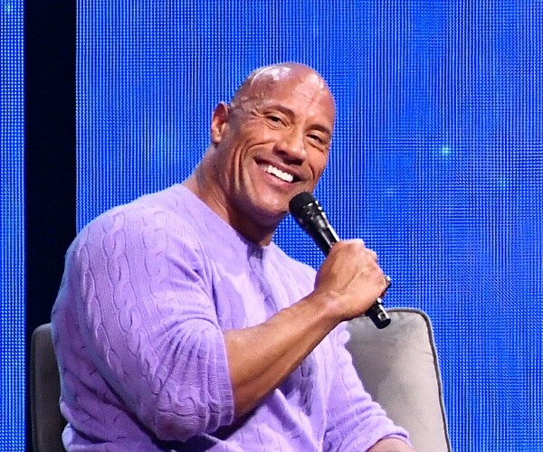 dwayne johnson sits onstage holding handheld mic