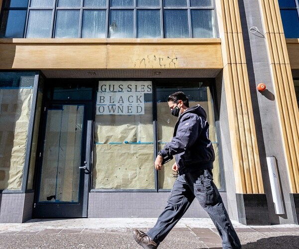 man walks by boarded up store