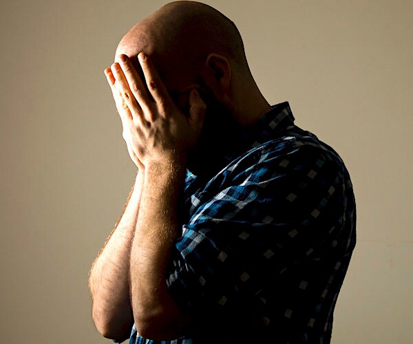 a depressed man buries his face in his hands