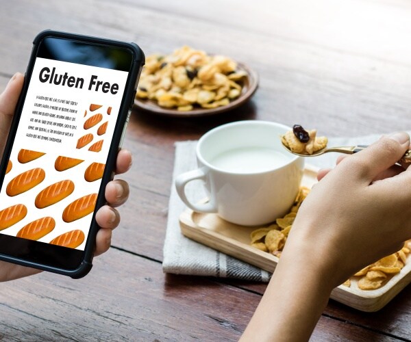 person eating breakfast and holding/reading phone with information about Celiac disease and eating gluten free