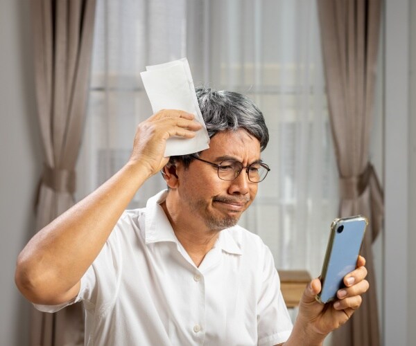 older man on phone, holding a bill, looking mad and frustrated