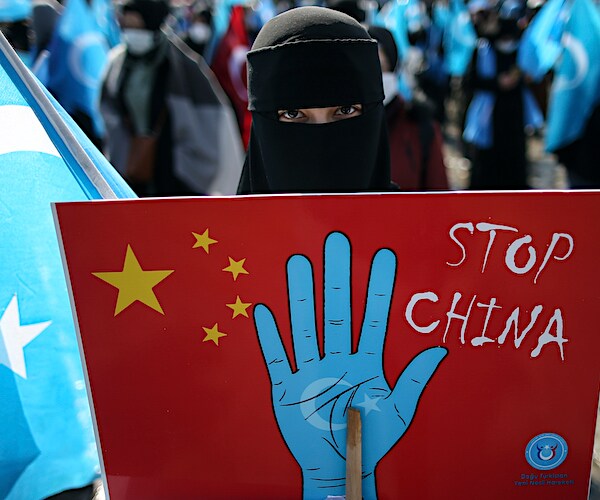 a protester in a burqa holds a sign reading stop china