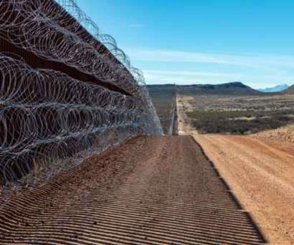 sections of a border wall are shown with razor wire on top