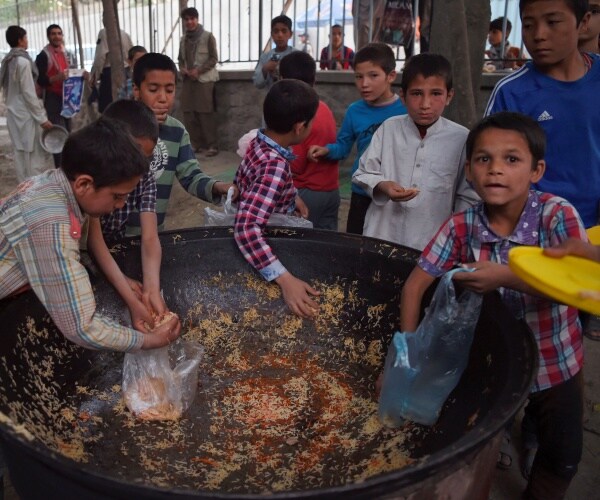 Afghan children collect rice from a big bowl