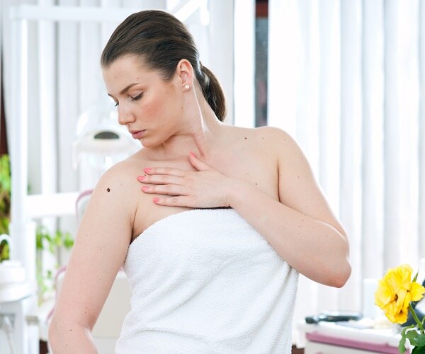 woman with towel on looking at shoulder where there is a mole