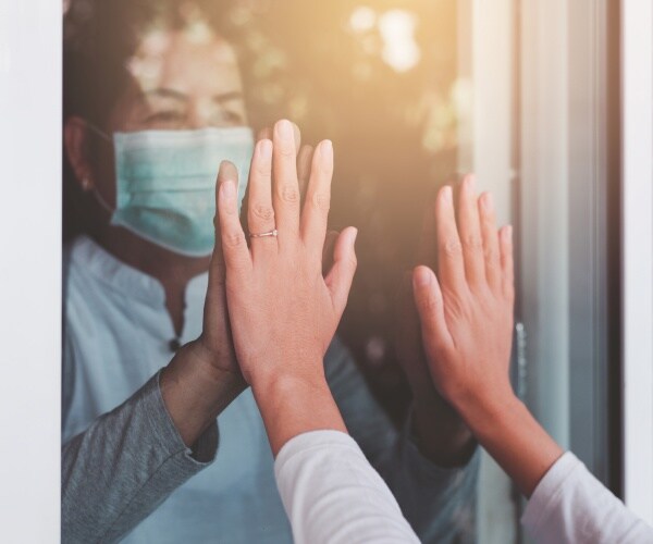 elderly woman with mask with hands up to glass of a person outside