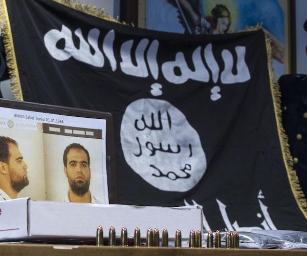 the black and white flag of the islamic state in syria stands behind a wanted poster of a terrorist