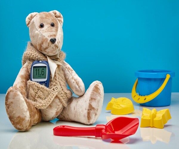 Stuffed bear with a glucose monitor in front pocket and kids sand toys around it