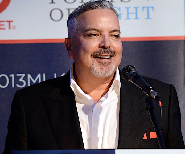 a man smiles while standing behind the podium at a news conference