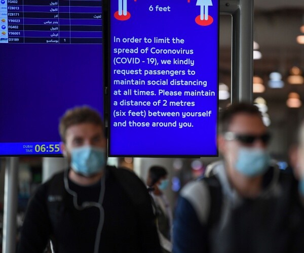 people walking by in blue face masks in front of a sign telling people to socially distance