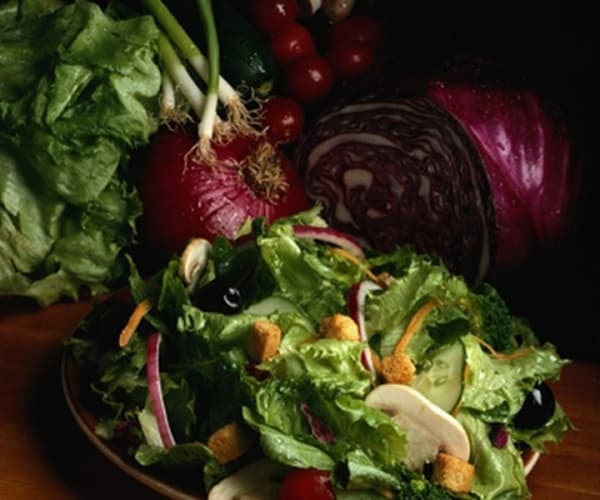 a salad with lettuce greens and other greens, vegetables behind it