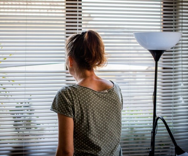 a woman in quarantine in her house looking in between slats of blinds