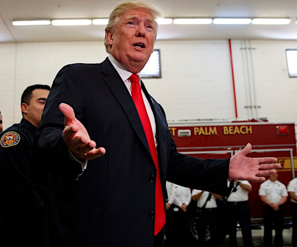 president donald trump extends both arms with palms up while walking through a throng of media