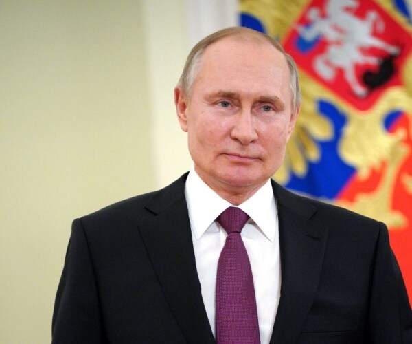 vladimir putin with dark suit, white shirt and burgundy tie with russian flag in background